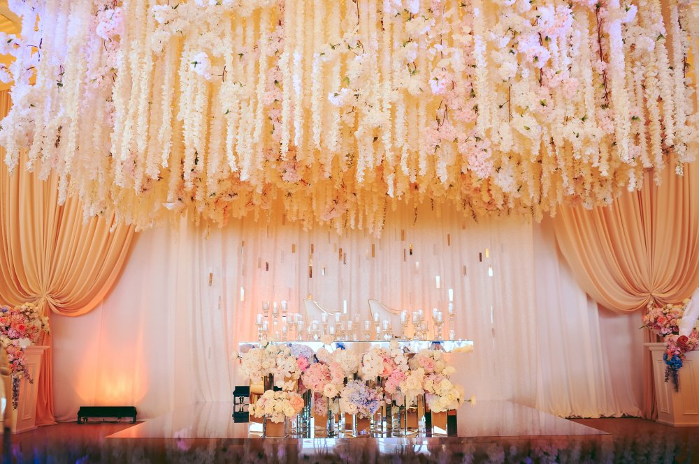 Indoor wedding backdrop with draped fabric and floral wall.