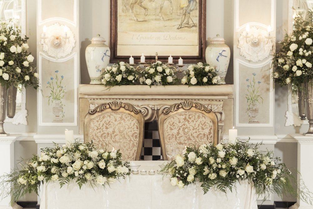 Luxury indoor wedding stage decorations with gold arches and roses.