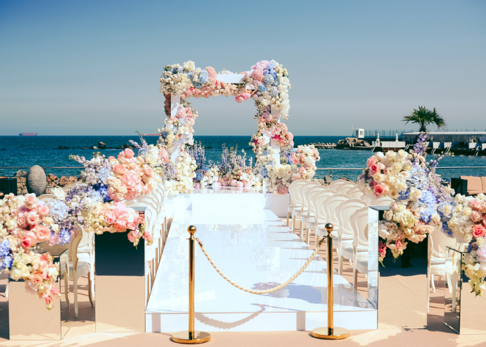 Beautiful wedding arch decorated with dusty rose flowers and soft dusty blue fabric drapes in an outdoor ceremony setting.