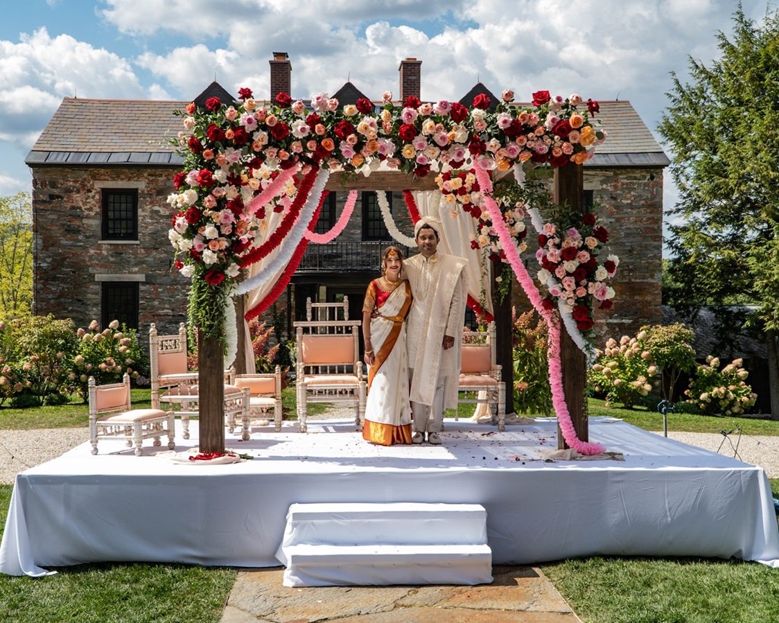 Copy of Copy of DSC00227 A classic floral centerpiece with white roses, eucalyptus, and soft pink peonies arranged in a crystal vase, placed on a round wedding table with candles — symbolizing elegance, romance, and timeless wedding décor.
