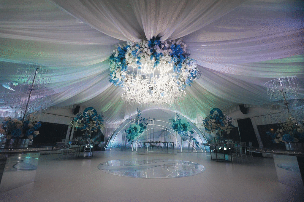 Elegant wedding reception hall decorated with ceiling drapes and warm fairy lights creating a luxurious, romantic ambiance for a modern celebration. Elegant wedding reception hall decorated with ceiling drapes and warm fairy lights creating a luxurious, romantic ambiance for a modern celebration.