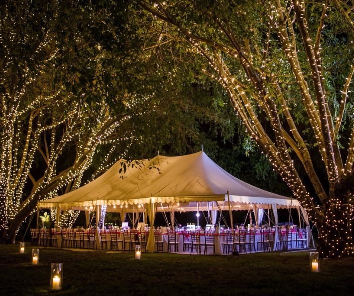 Outdoor tent wedding decor with string lights and drapery.